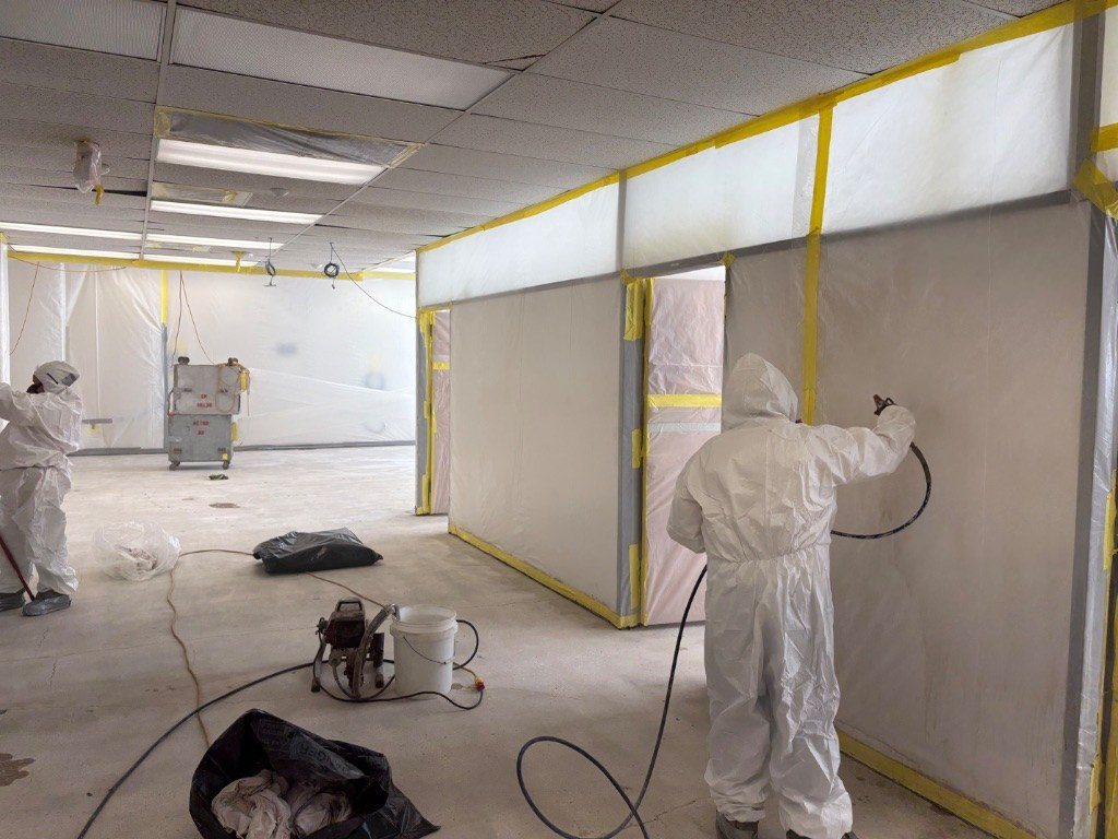 RETRO crew in protective suits working inside a large poly containment with a negative air machine
