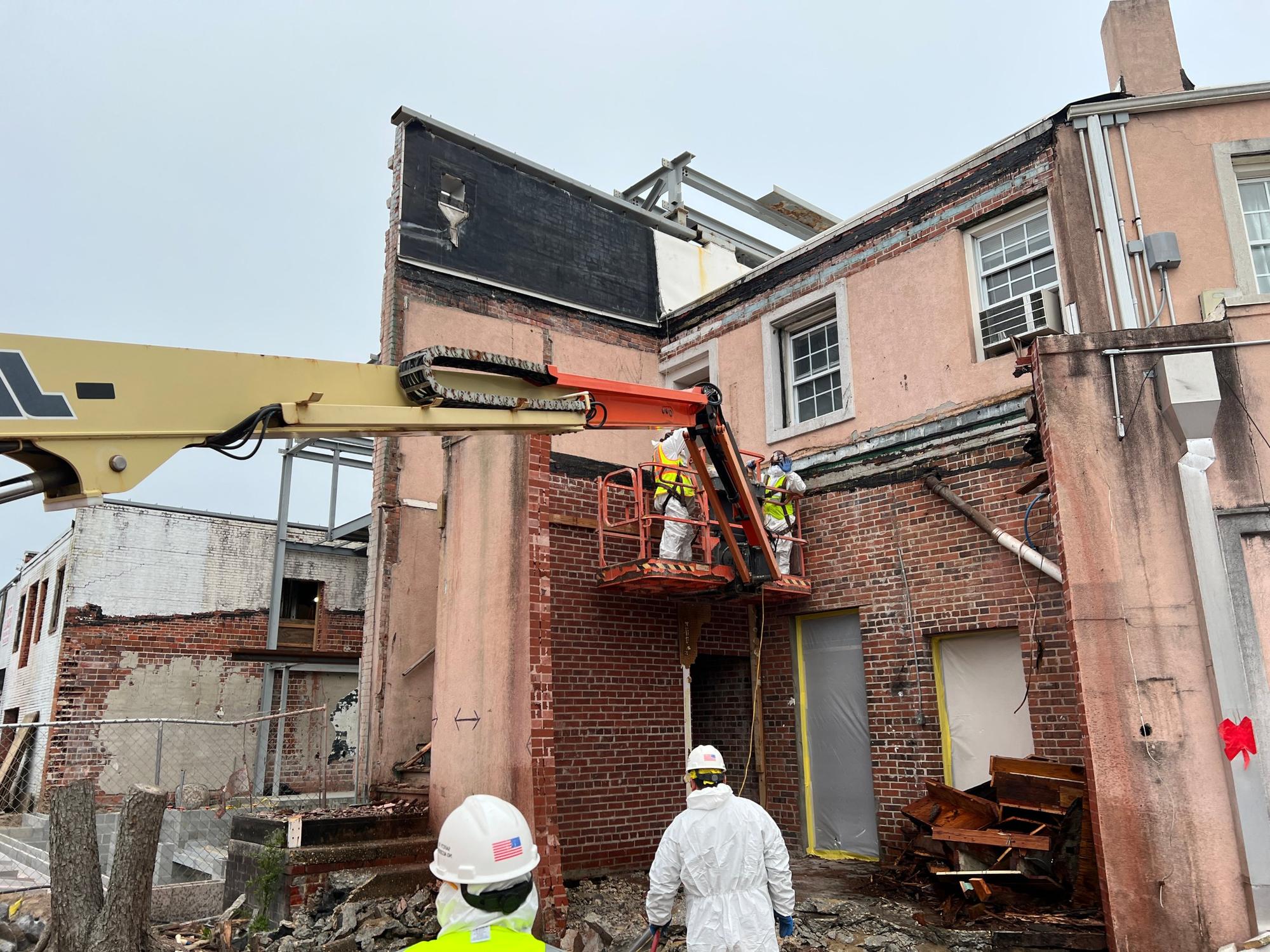 RETRO crew on a boom lift removing part of a brick and stucco building façade, with new steel framing behind
