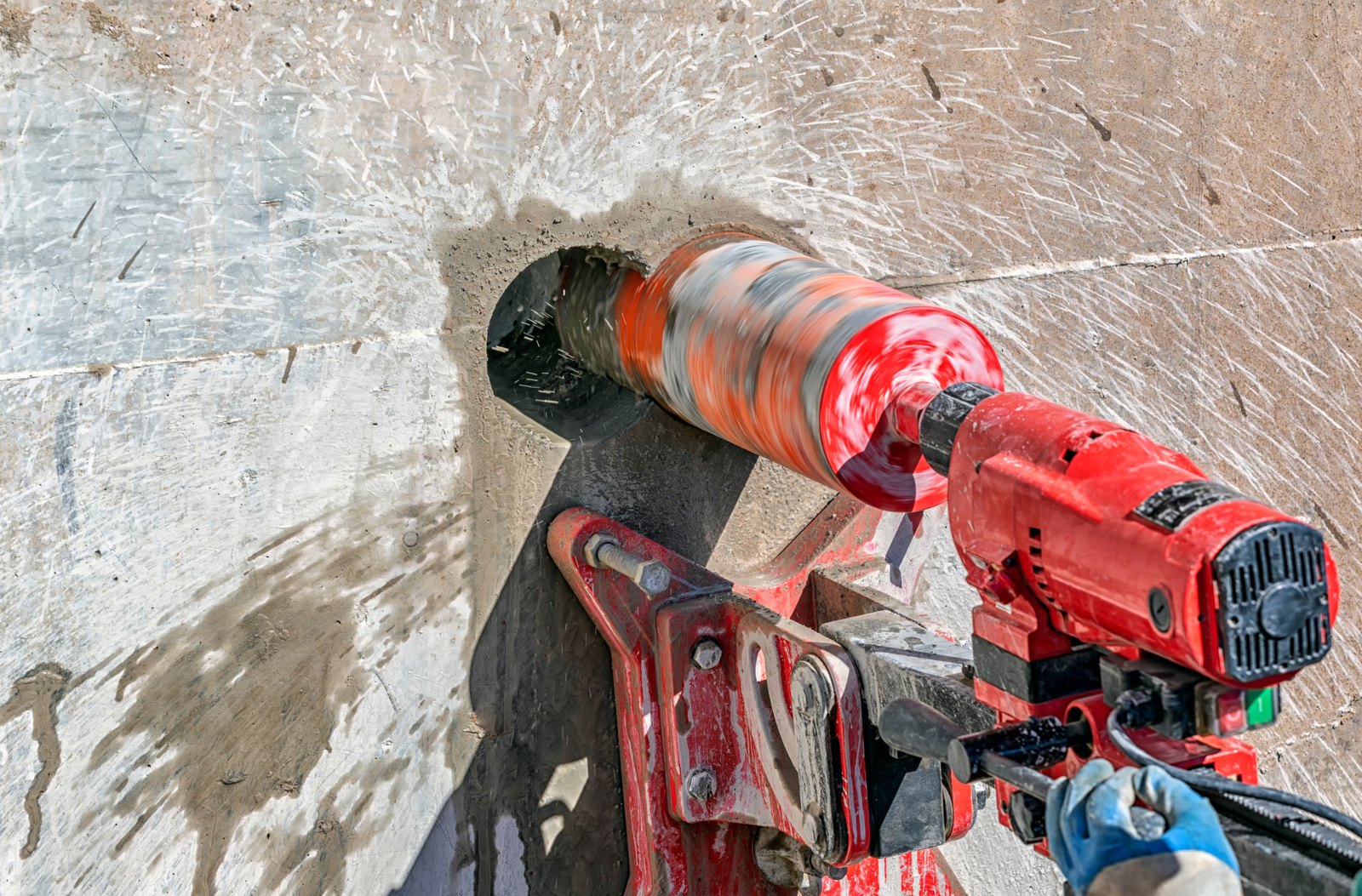 Diamond core drill mounted on a stand, coring through a concrete wall with water spraying from the bit