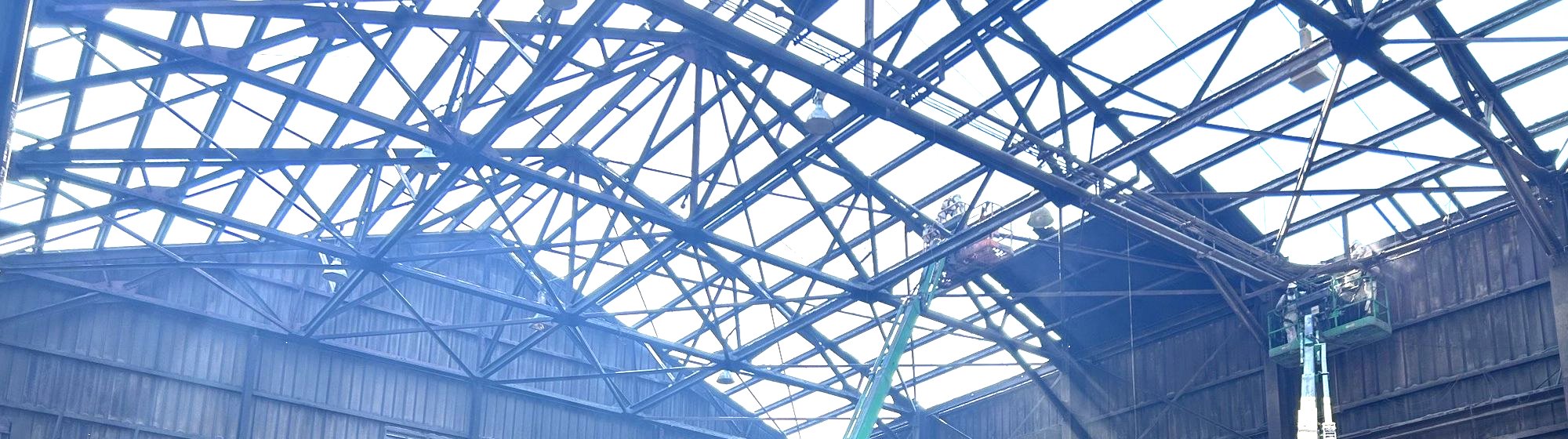 RETRO crews in protective suits on two boom lifts working at the exposed roof trusses of a large steel mill building
