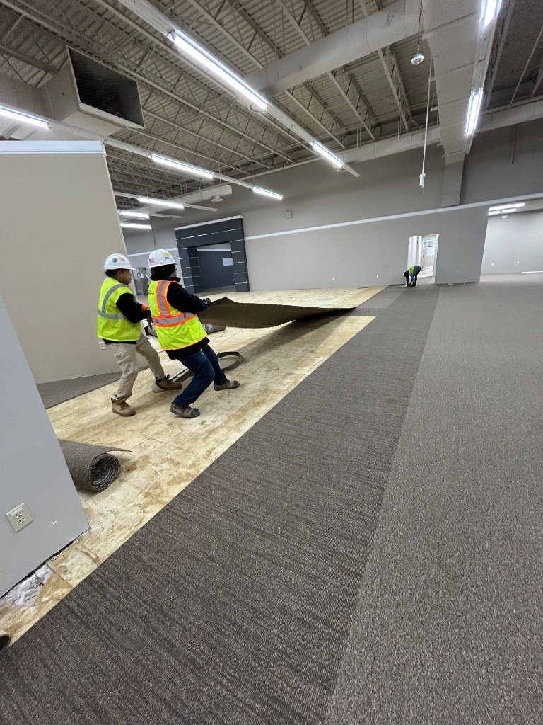 RETRO crew in hard hats and safety vests pulling up carpet across an open commercial floor