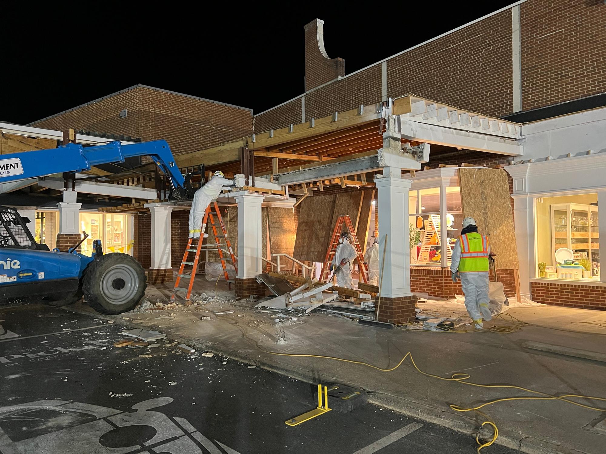 RETRO crew in protective suits removing a storefront canopy at night while the shops stay lit and open