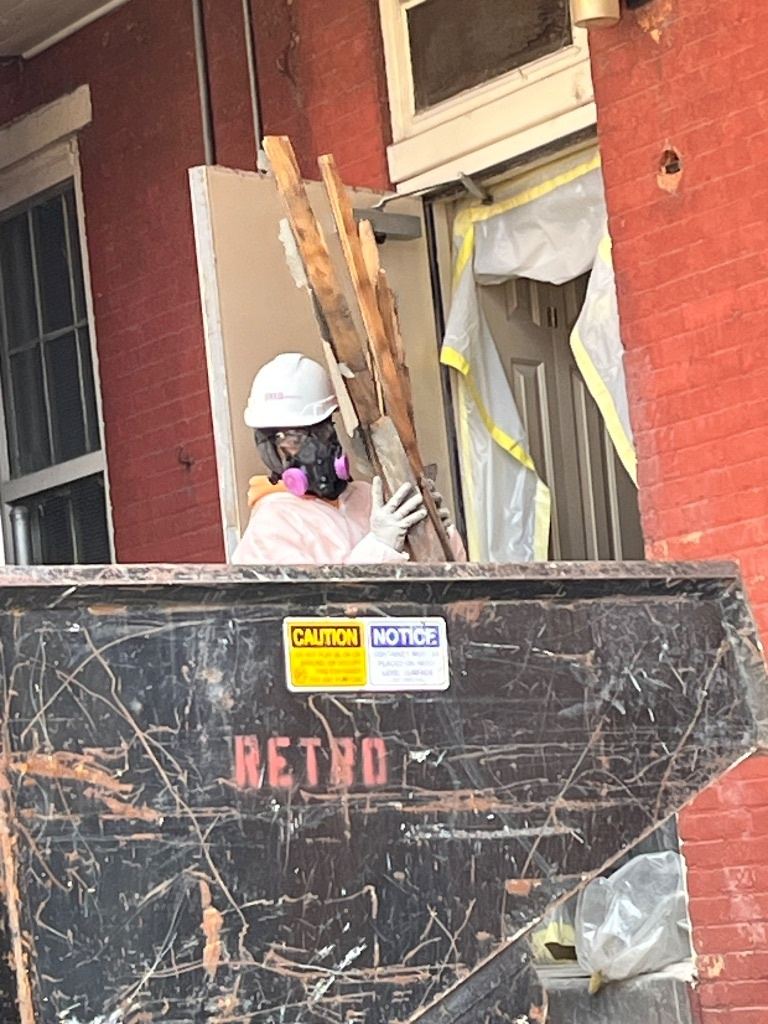 RETRO crew member in a hard hat and respirator loading wood debris into a RETRO dumpster outside a brick building