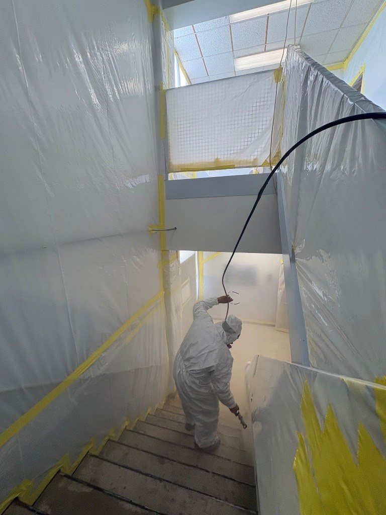 RETRO crew member in a protective suit spraying inside a stairwell fully lined with poly containment