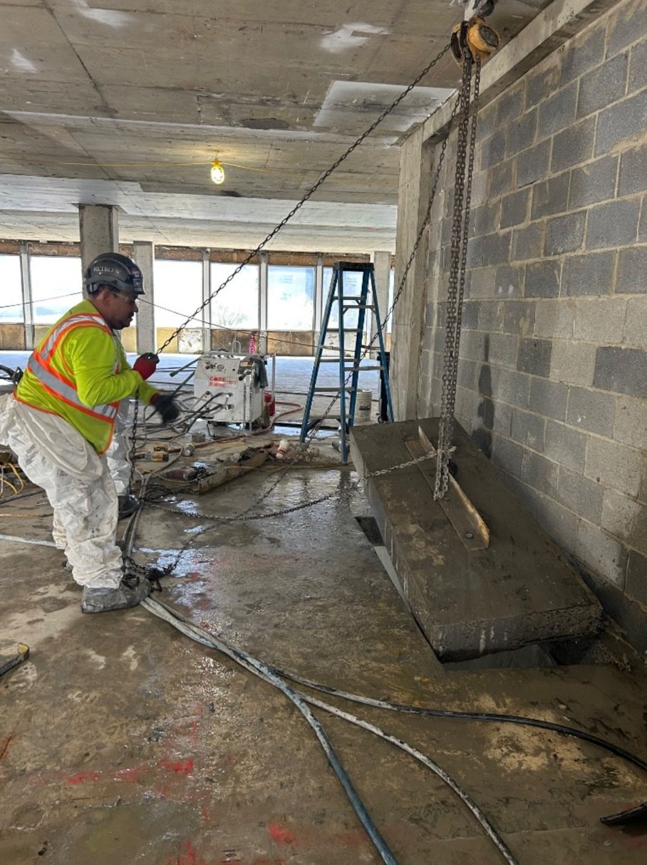 RETRO crew member guiding a saw-cut concrete slab section out of the floor with a chain hoist