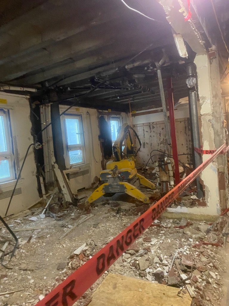 The BROKK® remote-controlled machine working beneath temporary steel shoring behind danger tape
